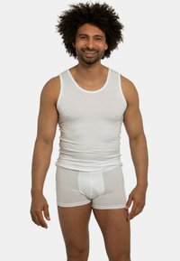 Canottiera bianca di cotone e slip boxers su un uomo sorridente, che mostra un design aderente con una texture liscia e senza motivi.