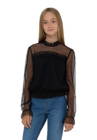 Blusa nera con pois, maniche lunghe trasparenti, scollatura arricciata e vita elasticizzata. Indossata con jeans azzurri chiari per creare un contrasto.
