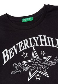 Czarna bawełniana koszulka z białym graficznym napisem "Beverly Hills Los Angeles" w kształcie gwiazdy, z zieloną metką z napisem "United Colors of Benetton."