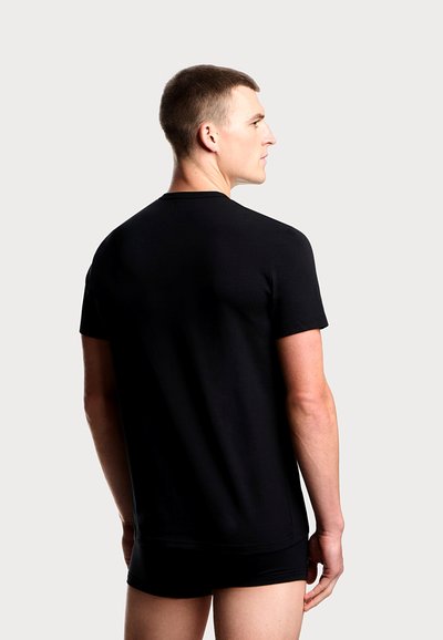 Černé tričko s krátkým rukávem z hladké tkaniny, s klasickým kulatým výstřihem a volným střihem. Model zobrazen zezadu.