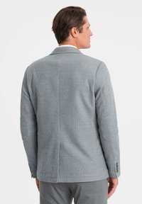Grau Blazer aus strukturiertem Stoff, taillierte Passform und Ellbogenpatches. Verfügt über einen Schlitz und Knopfakzente an den Ärmeln.