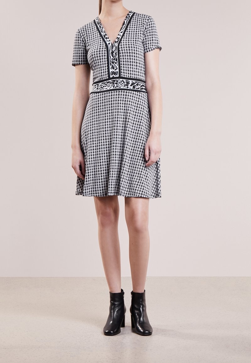 Zwart-witte houndstooth jurk met een V-hals, korte mouwen, een getailleerde taille en een uitlopende rok. Gepaard met zwarte enkellaarsjes.