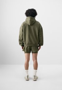 Olivengrøn hoodie med en rummelig hætte, korte olivenfarvede shorts og hvide sokker med detaljer. Casual pasform, struktureret stof, enkelt design.