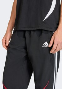 Melnā sporta augšdaļa ar vertikālām svītrām un baltu akcentu. Melni bikses ar baltām svītrām un sarkanu detaļu. Adidas logotips uz biksēm.