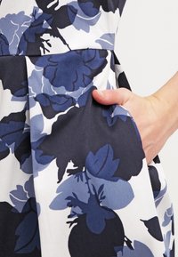 Vestido floral con una gama de colores en azul marino y celeste, confeccionado en una tela suave con un detalle de bolsillo y un diseño plisado.