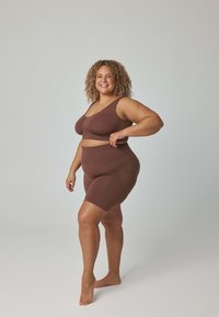 Brązowy bezszwowy komplet sportowy z biustonoszem i szortami, charakteryzujący się miękką fakturą oraz minimalistycznym designem z szerokimi ramiączkami i średnim stanem.