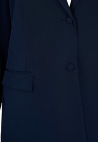 Tummansininen bleiseri, jossa on sileä kangas, kaksi nappia, pyöreä kaulus ja yksi läppätasku vasemmalla puolella.