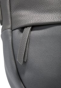 Primo piano di un angolo di una borsa in pelle e tessuto grigia con un pratico zip in pelle abbinata.