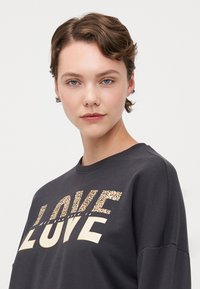 Dark gray sweatshirt featuring "LOVE" printed in a mix of leopard print and solid cream letters. Crew neckline and relaxed fit.