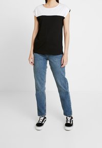 Czarna i biała koszula krótki rękaw z okrągłym dekoltem, zestawiona z jasnoniebieskimi dżinsami i czarnymi trampkami z białą podeszwą.