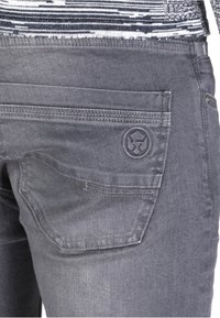 Vaqueros de mezclilla gris con un bolsillo trasero que presenta un logo de marca circular, costuras en contraste y un acabado de tela texturizada.
