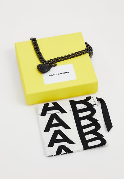 Gelbes quadratisches Kästchen mit schwarzer Kette und Herzanhänger; schwarz-weißes Täschchen mit fetten Buchstaben. Marc Jacobs Branding auf der Verpackung.