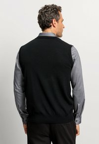 Schwarzer ärmelloser Pullover über einem grauen Langarmshirt. Der Pullover hat eine glatte Textur, einen gerippten Saum und ein V-Ausschnitt-Design.