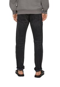 Black denim jeans with a straight-leg fit. Features back pockets, slight whiskering, and rolled cuffs. Styled with black slip-on shoes.