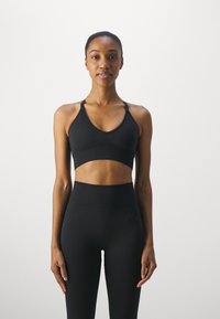 Sutiã desportivo preto com decote em V e alças largas, combinado com leggings de cintura alta com textura canelada e padrões subtis.