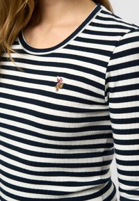 Stripet langermet topp i marineblå og hvit ribbet stoff, med en liten brodert detalj av en leken figur på brystet.