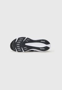 Semelle en caoutchouc noir et blanc d'une chaussure de sport avec un motif de bande de roulement texturé, présentée sur un fond clair.