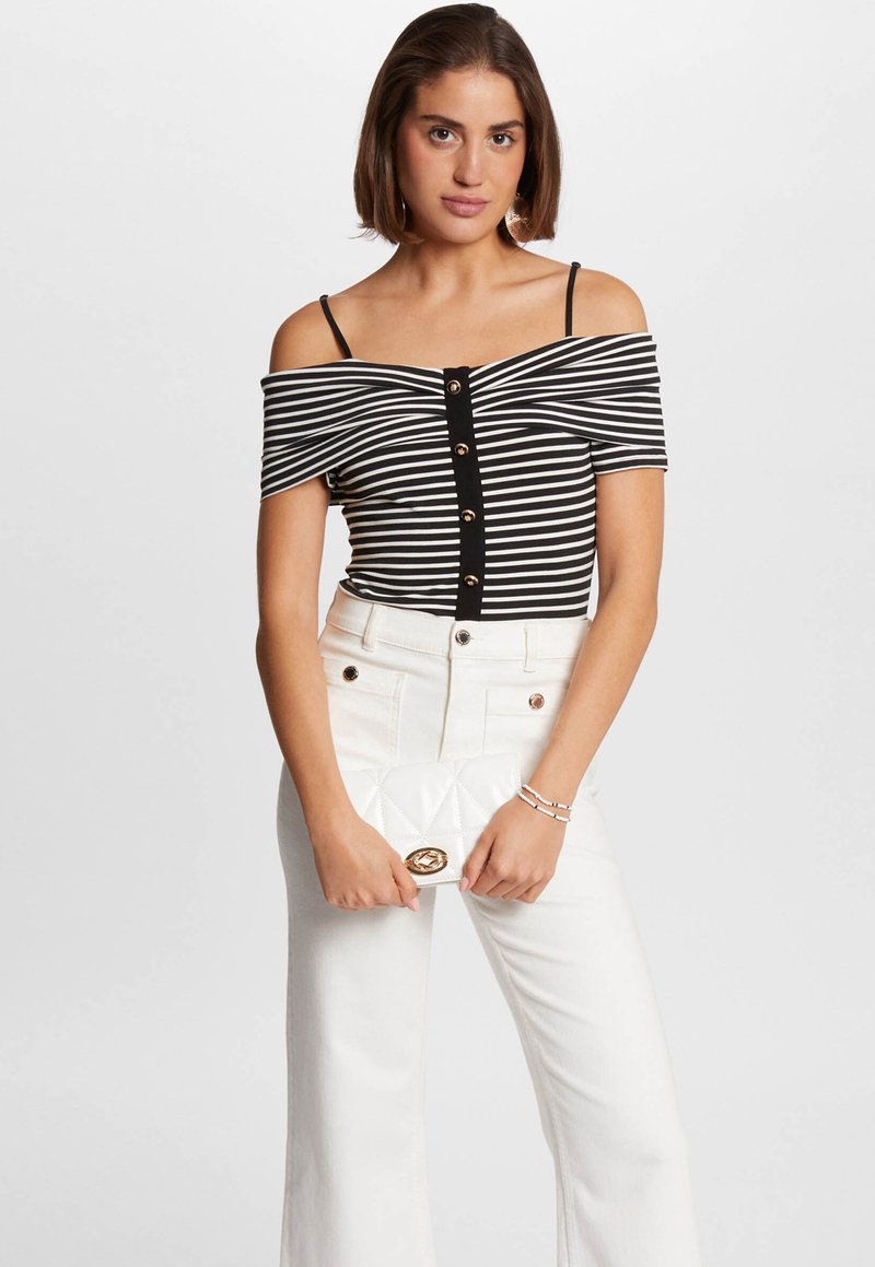 Top negro y blanco a rayas sin mangas con detalles de botones, combinado con pantalones de pierna ancha blancos de cintura alta y un bolso acolchado blanco.