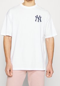 Biała bawełniana koszulka z luźnym krojem, z ciemnogranatowym logo NY na piersi. Krótkie rękawy i okrągły dekolt.
