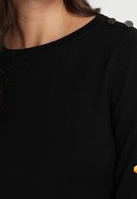 Maglione nero con finitura testurizzata, dotato di un collo rotondo e bottoni metallici decorativi sulla spalla.
