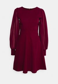 Robe bordeaux avec longues manches bouffantes transparentes, taille cintrée, encolure ronde et jupe évasée sur un fond clair.