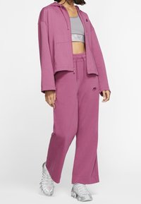 Roze hoodie met een voorzak en verstelbare koorden, gecombineerd met bijpassende roze joggers met een klein logo. Zilverkleurige sport schoenen.