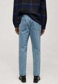 Persona con jeans rectos de color azul claro con bolsillos traseros, zapatos negros y una camisa de manga larga a cuadros en tonos azul oscuro y negro.