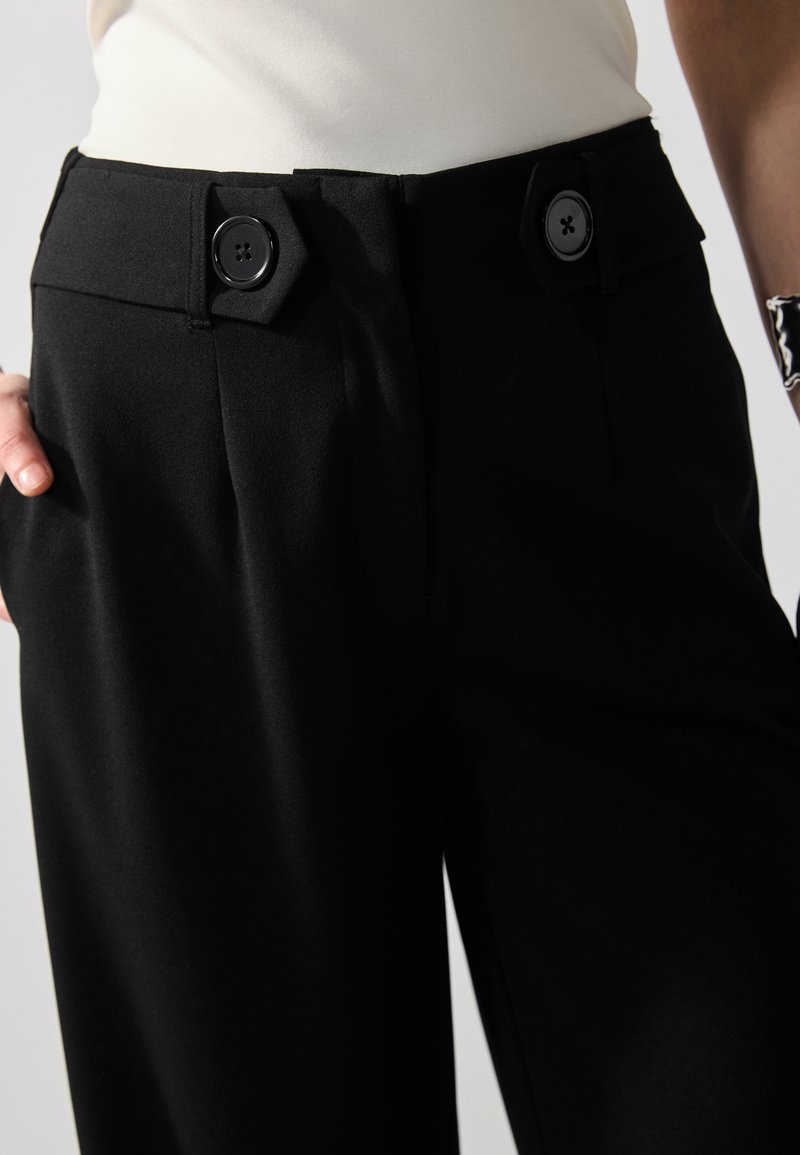 Pantaloni neri realizzati in tessuto liscio, con due bottoni neri in vita, tasche angolate e una silhouette sartoriale.