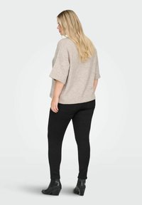 Maglia beige oversize con maniche corte, abbinata a jeans neri aderenti e stivaletti neri alla caviglia. La maglia ha una texture morbida e una vestibilità comoda.