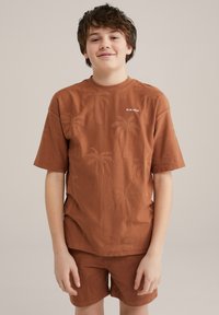 Brun bomullströja och matchande shorts med präglade palmträmönster, rund halsringning och avslappnad passform. "BLUE RIDGE"-logotypen visas på bröstet.