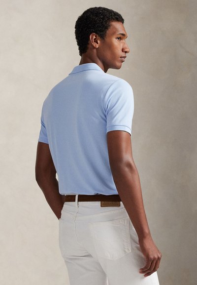 Ανοιχτό μπλε πόλο πουκάμισο με κοντά μανίκια, υφασμάτινη υφή και κλασικό γιακά. Συνδυασμένο με λευκό παντελόνι και καφέ ζώνη.