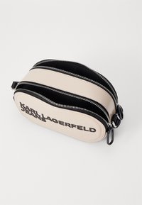 Borsa jeans Karl Lagerfeld, forma ovale, in ecopelle beige con zip nere, con un audace marchio nero su un lato. Due scomparti con zip.