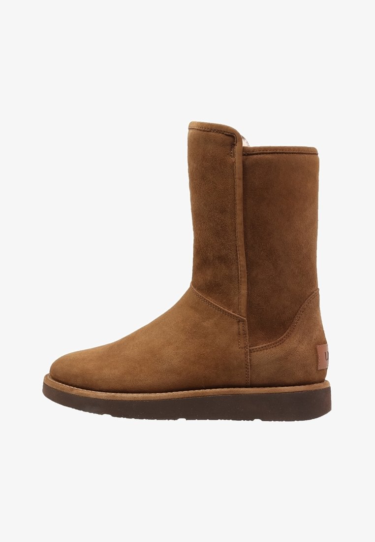 Botte en daim marron mi-mollet avec semelle plate et bout arrondi, coutures visibles et languette à l'arrière.