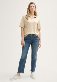 Polo de manga corta beige, vaqueros de pierna recta azul denim y zapatillas blancas. Tejido suave, corte relajado, cuello clásico y estilo casual.
