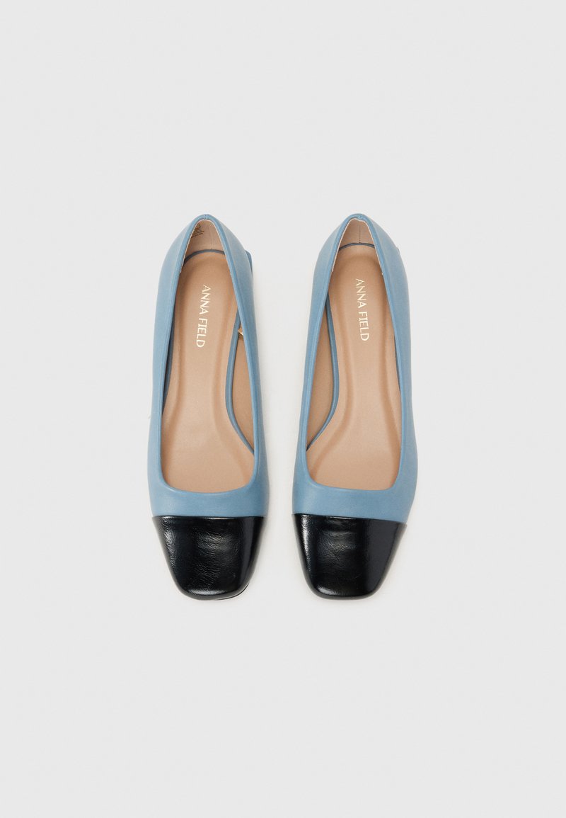 Bottines plates bleu clair avec un design à bout carré, dotées d'un capuchon en cuir noir sur le bout et d'une texture lisse. Nom de la marque à l'intérieur.