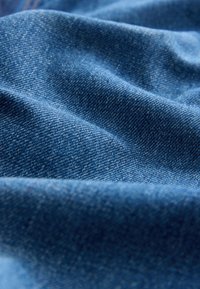 Nahaufnahme von blauem Denimstoff mit sichtbarer Webstruktur und weichen Falten, die sanfte Schatten erzeugen.