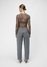 Top de leopardo marrón transparente de manga larga, combinado con jeans de mezclilla de tiro alto y lavado claro, y sandalias negras de tacón.