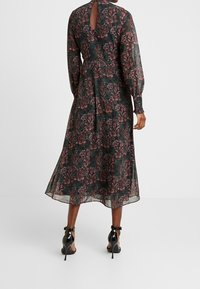 Pitkähihaiset kukkakuosiset mekko, jossa on tumman vihreä tausta, kevyt kangas ja avaus selässä. A-linjainen siluetti.