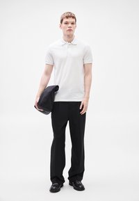 Λευκό πόλο με κοντά μανίκια και γιακά, μαύρο φαρδύ παντελόνι, μαύρη τσάντα και μαύρα παπούτσια. Ομαλό ύφασμα και άνετη εφαρμογή.