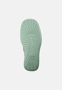 Grön gummisko sula med texturerade ribbor och ordet "CAMPE" präglat. Storlek 38 angiven. Solstrålemönster strålar ut från mitten.