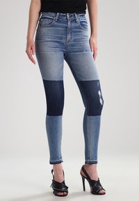Jeans ajustados en varios tonos de denim azul, con un diseño de patchwork en dos tonos y detalles desgastados cerca de la rodilla.