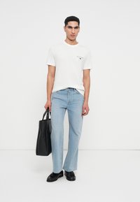 Tricou alb cu mânecă scurtă și logo, blugi drepti de culoare albastru deschis, geantă mare neagră și pantofi negri. O ținută simplă și casual.