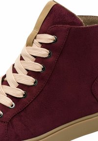 Burgundy high-top sneaker made of soft suede, featuring beige laces, black eyelets, and a tan rubber sole. Smooth texture with stitching detail.
