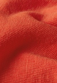 Tejido suave y texturizado en un vibrante color naranja, que exhibe un patrón de punto con costuras visibles y una sensación cálida y acogedora.