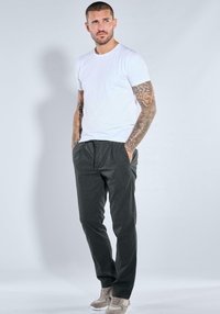 Dark gray, relaxed-fit trousers with elastic waistband, paired with a plain white t-shirt. Model wears beige sneakers. Smooth texture.