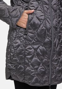 Grijze gewatteerde jas met een gladde textuur, voorzien van zijzakken, een ritssluiting en knoopaccenten op de mouwen.