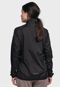 Schwarze, leichte Jacke mit Stehkragen, elastischen Bündchen und einer glatten, wasserabweisenden Textur. Mit einem Logo am Ärmel.