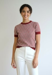 Czerwono-biały sweter z krótkim rękawem w paski, z okrągłym dekoltem i ściągaczami na rękawach, zestawiony z białymi, dopasowanymi spodniami.