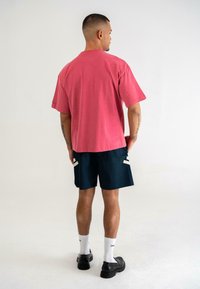 Růžové bavlněné tričko s krátkými rukávy, spojené s námořnickými šortkami se bílými akcenty. Černé boty a bílé ponožky dokončují outfit.