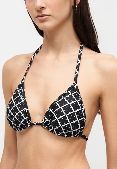 Femme portant un haut de bikini triangulaire à motif noir et blanc avec des bretelles halter autour du cou et des liens sur les côtés.